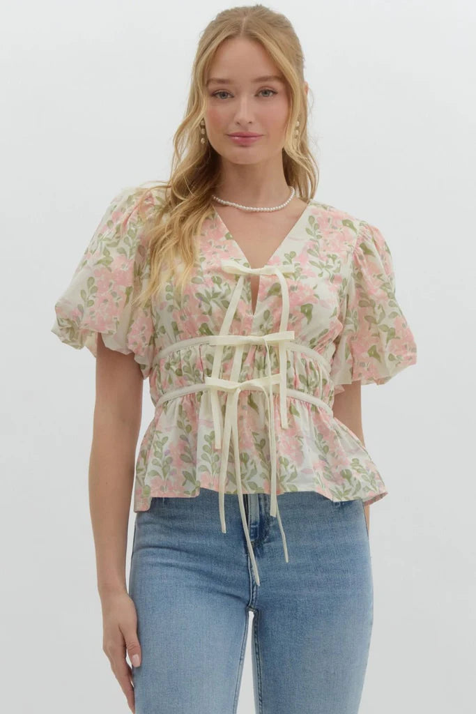 Feminine floral puff-sleeve blouse with lace-up front, pastel floral print, and peplum silhouette. Perfect for romantic and casual outfits.