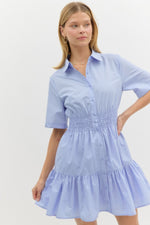 light blue short-sleeve shirt dress with a collared neckline, button-down front, and smocked waist. The dress has a tiered skirt and a relaxed yet flattering fit.