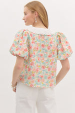 pastel floral puff-sleeve blouse with a delicate eyelet lace collar and button-down front. The top features a soft, textured fabric with a romantic vintage-inspired design.