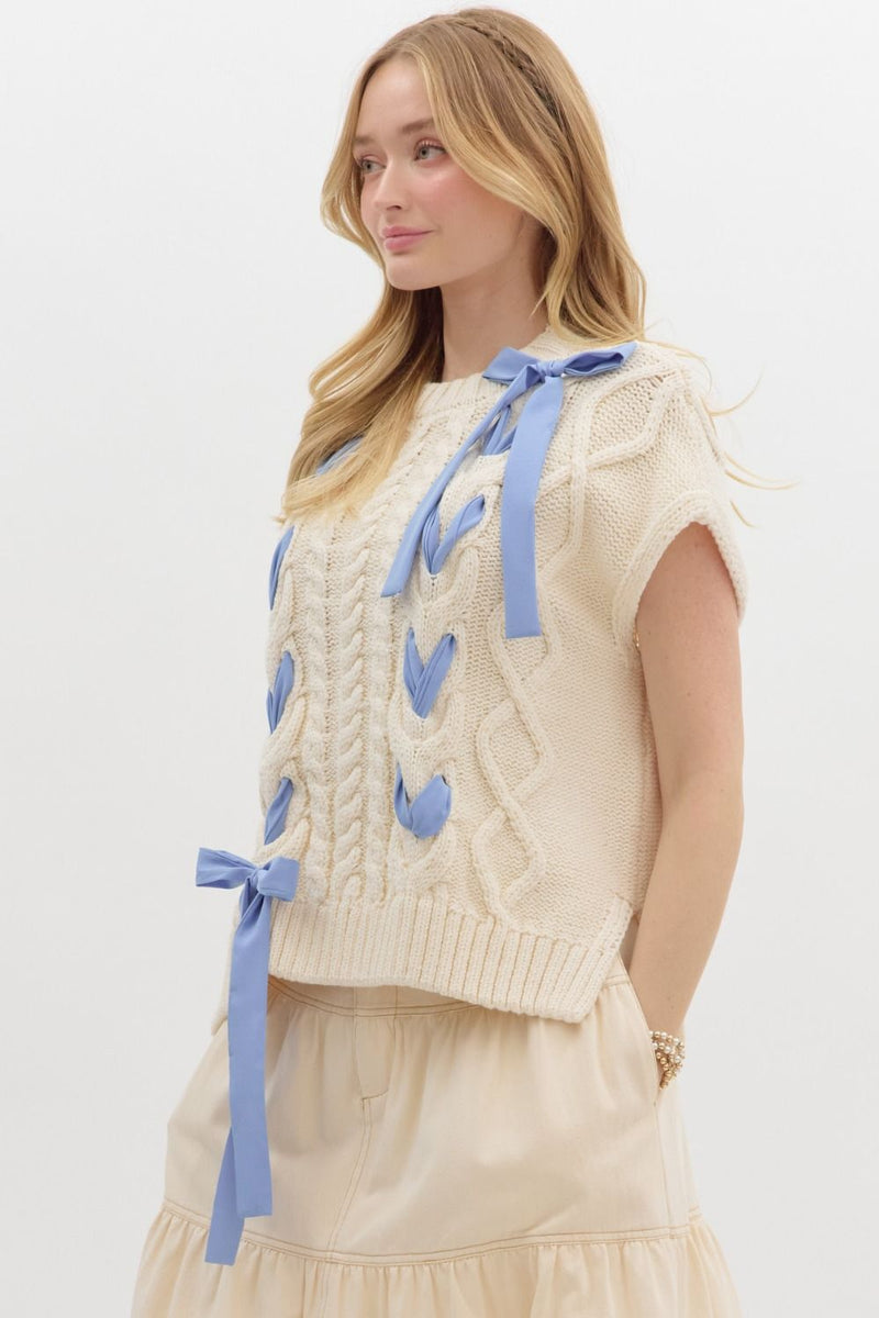 Cream knit sweater with blue ribbon details and cable knit pattern