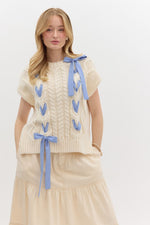 Cream knit sweater with blue ribbon details and cable knit pattern